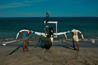 Rear view of man pushing outrigger into sea at beach