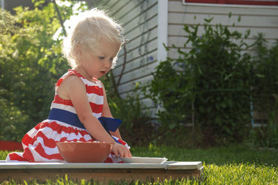 Pretty curly little girl seating in garden and eating berries from the plate.