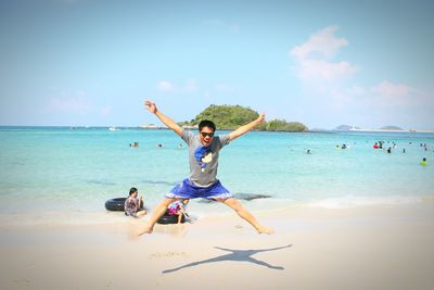 Full length of excited man jumping at beach against sky