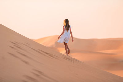 Woman standing on sand dune in desert against sky