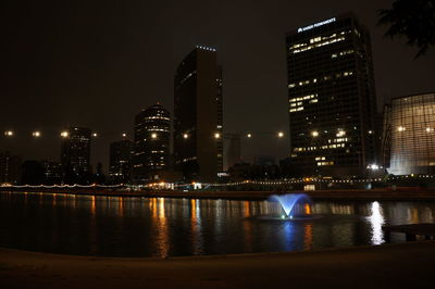 Illuminated buildings by river against sky at night