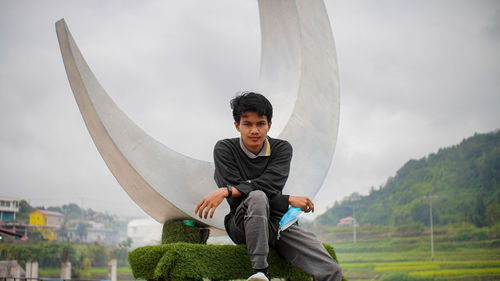 Portrait of young man sitting against sky