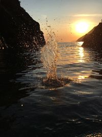 Water splashing on sea against sky during sunset