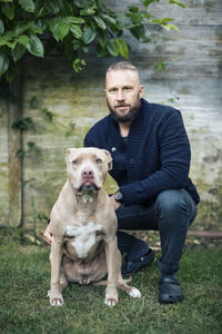 Portrait of man crouching by american pit bull terrier at yard