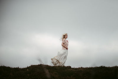 Bride standing on grass against sky