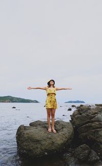 Full length of woman standing on rock at sea shore against sky