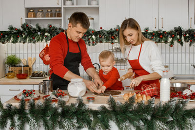 Happy young family in the festive kitchen is very busy with cooking the dough on a white table. 