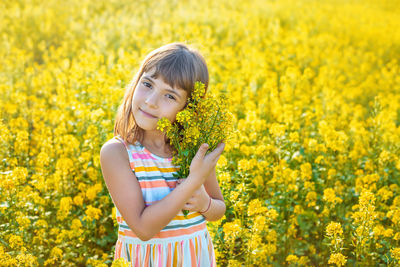 Portrait of cute girl holding flowers while standing in field