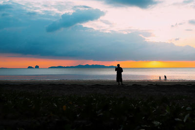 Silhouette people standing on beach against sky during sunset