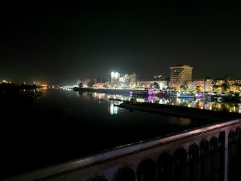 Illuminated buildings by river against sky at night