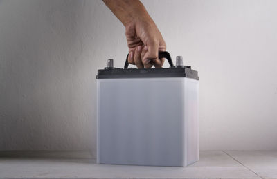 Cropped hand holding car battery against wall