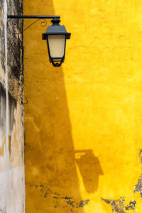 Low angle view of lighting equipment hanging against yellow wall