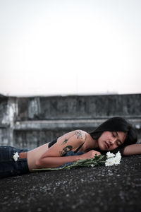 Beautiful woman with flower lying on floor against sky