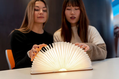 Multi-ethnic female couple of girlfriends are looking at a magical bright book indoors