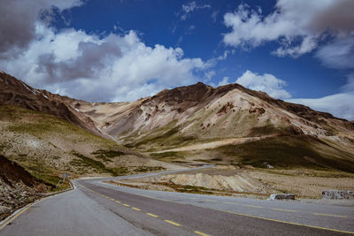 Empty road leading towards mountains against sky