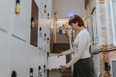 Side view of teenage girl keeping book in locker at corridor