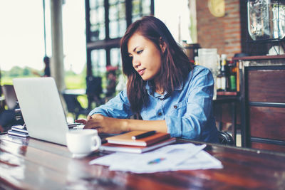 Young woman using phone while sitting on table