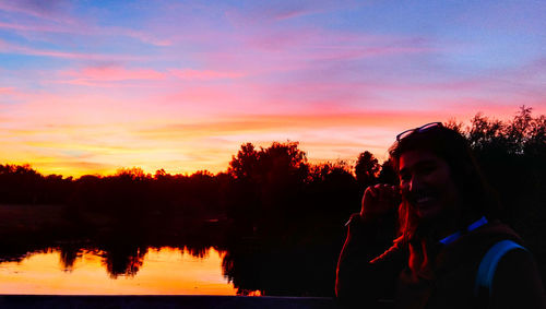 Silhouette woman by lake against sky during sunset