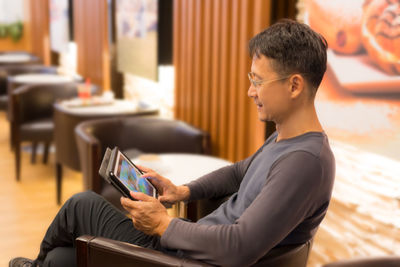 Side view of mid adult man using digital tablet while sitting on chair