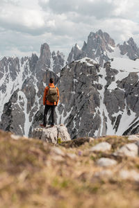 Back view of male traveler in warm clothes standing on rock and observing snowy dolomites mountains on sunny day