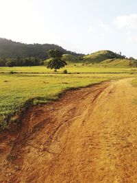 Dirt road amidst field against sky