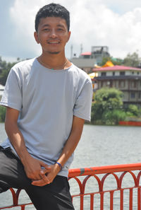 Portrait of a ladakhi young guy sitting on safety barrier by lake and looking at camera 