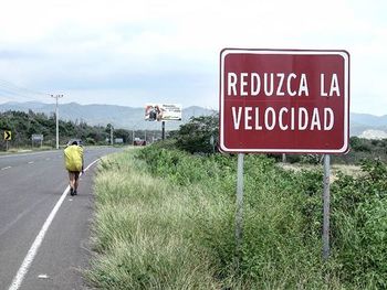 Road sign on field against cloudy sky