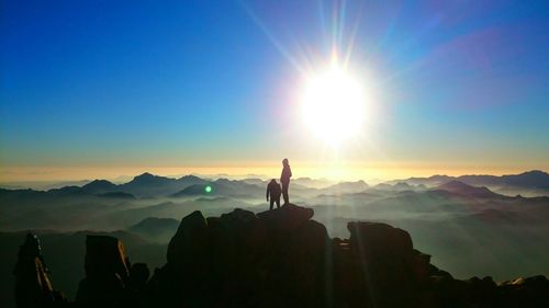 Silhouette people standing on rocky mountains against sky