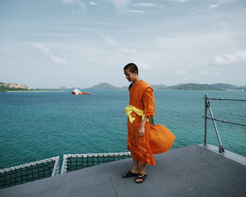 Monk standing on boat by sea against sky