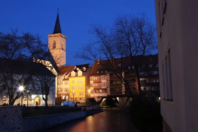 Illuminated buildings by canal against sky at dusk
