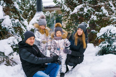 Mom with dad and son and daughter in winter in yard near snow-covered christmas