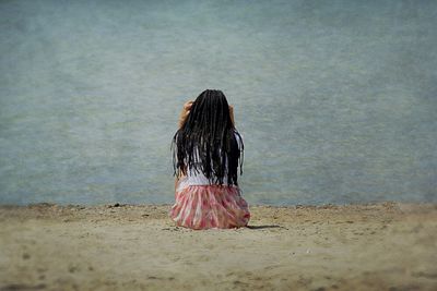 Rear view of woman with braided hair sitting at beach