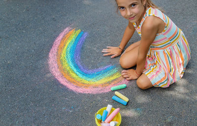 Girl drawing rainbow with chalk on sidewalk