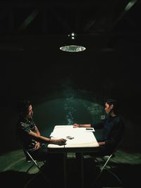 Young men holding cigarette while sitting at table in darkroom