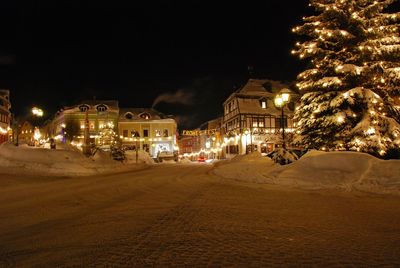 Illuminated street amidst buildings against sky at night