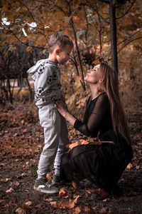 Side view of mother looking at cute son while crouching on field in park during autumn