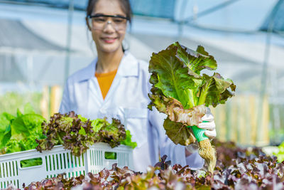 Smiling botanist holding vegetables at greenhouse