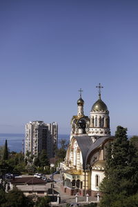 Church by buildings against clear blue sky