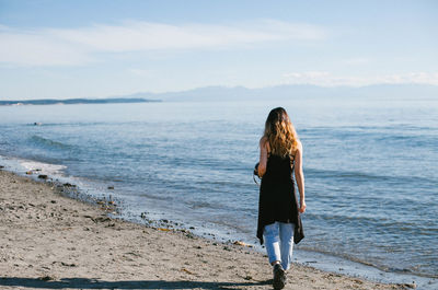 Rear view of woman standing at beach against sky