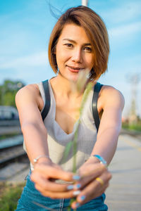 Portrait of woman holding plant while sitting against sky