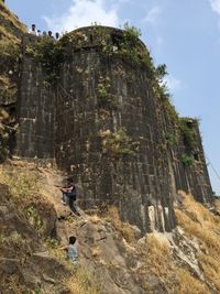 Low angle view of man climbing on mountain against sky