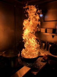 Cropped hand holding cooking pan with fire in kitchen