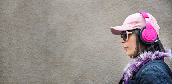 Side view of woman wearing sunglasses and headphones against wall