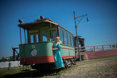 Full length of woman standing on old tram amidst field against blue sky