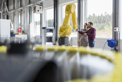 Businessman and woman having a meeting in front of industrial robots in a high tech company