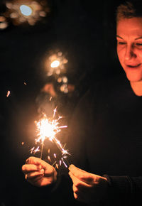 Smiling woman holding illuminated sparklers at night