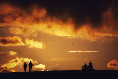 Silhouette people standing on land against sky during sunset