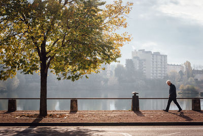 Side view of man walking on footpath by river in city