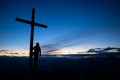 Silhouette men standing on cross against sky during sunset