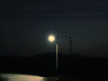 Illuminated street light against sky at night